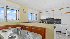 A kitchen with a dining area, white cabinets, a clock, and a window with a view. - Holiday Home 'Finca Tolombreo Casa Gabriel' in Cudillero (Cudillero)