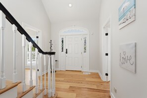A hallway with a wooden floor, white walls, a staircase with white balusters, and a white door with glass panels. - 153 Mooring Buoy: Lowcountry Modern Home w/Private Pool, Walk to Beach (Hilton Head Island)