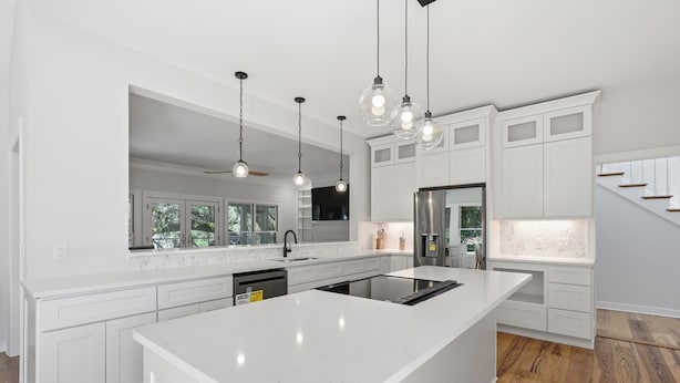 Una cocina moderna con armarios blancos, una isla grande, luces colgantes y vistas al exterior.