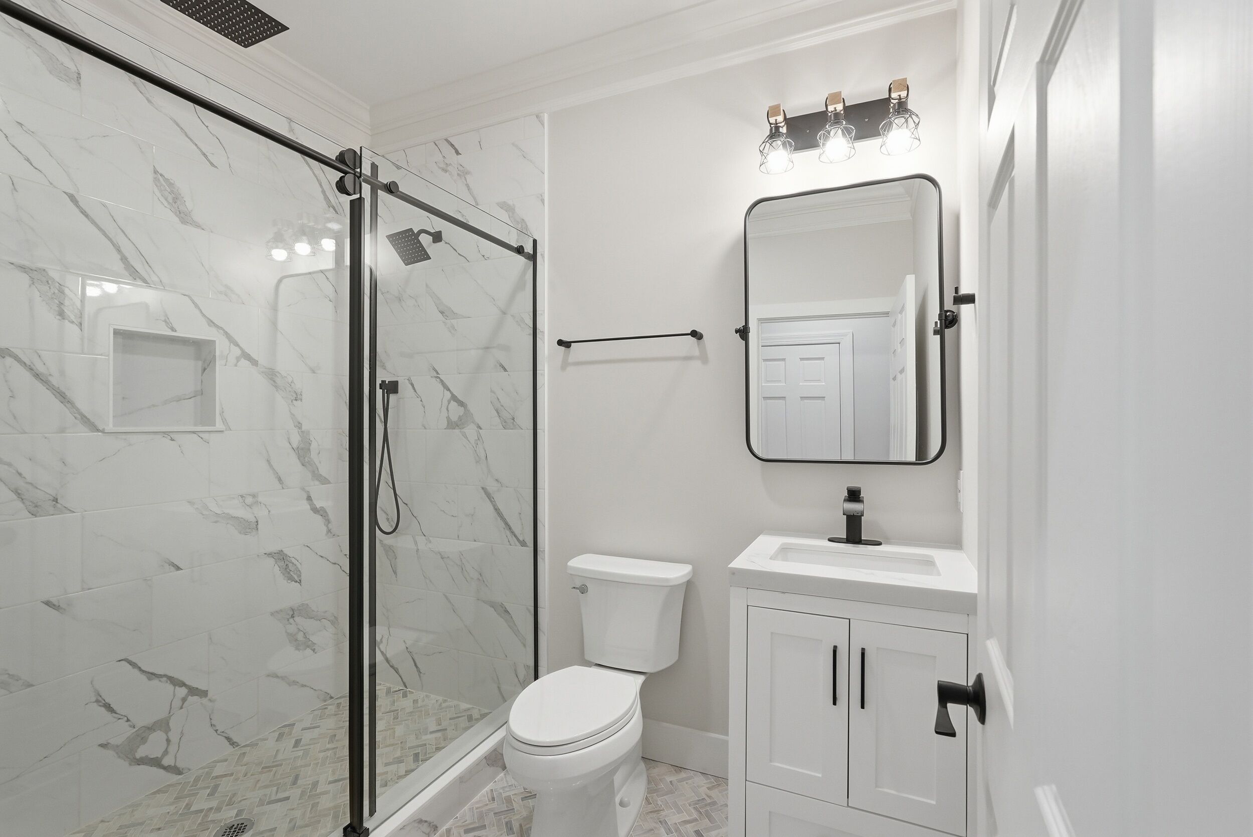 A bathroom with a glass-enclosed shower, a toilet, a sink, and a mirror.