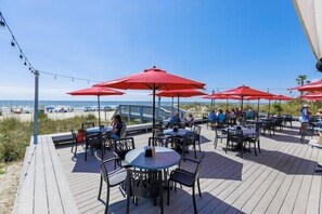 An outdoor deck with tables and chairs, red umbrellas, and a view of the beach. - 153 Mooring Buoy: Lowcountry Modern Home w/Private Pool, Walk to Beach (Hilton Head Island)