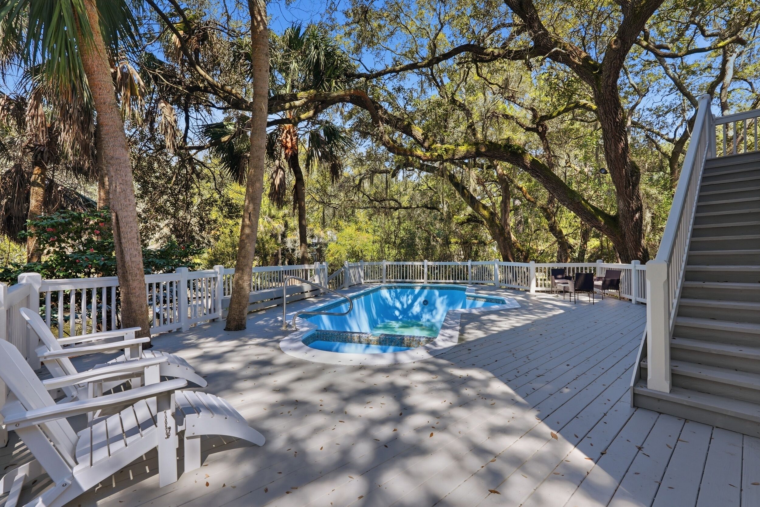 Une terrasse en bois avec une piscine, des rampes blanches et des sièges d’extérieur.