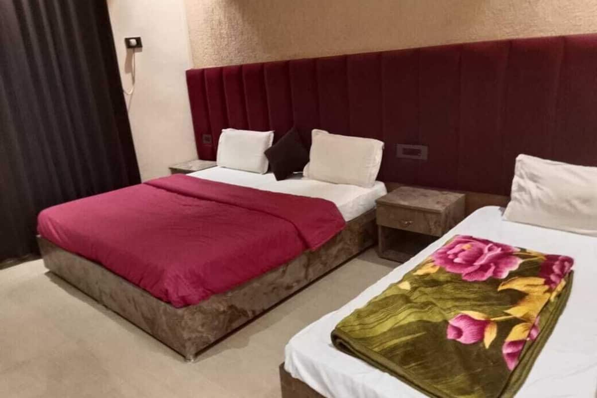 A hotel room with two beds, a red headboard, a nightstand, and a floral bedspread.