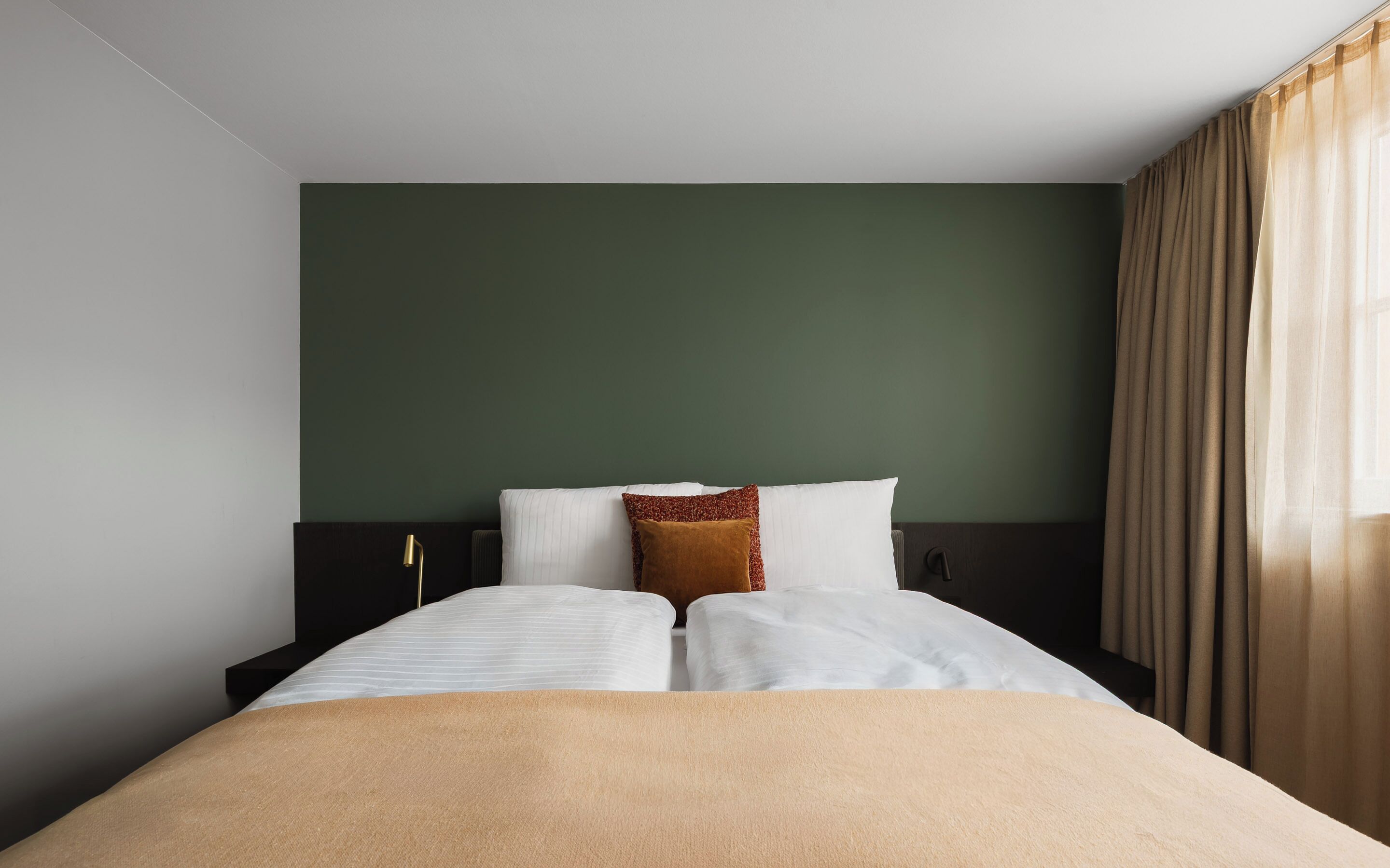 A hotel room with a bed, a nightstand, a lamp, and a window with curtains.