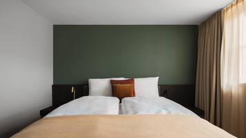 Een hotelkamer met een bed, nachtkastje, lamp en raam met gordijnen.