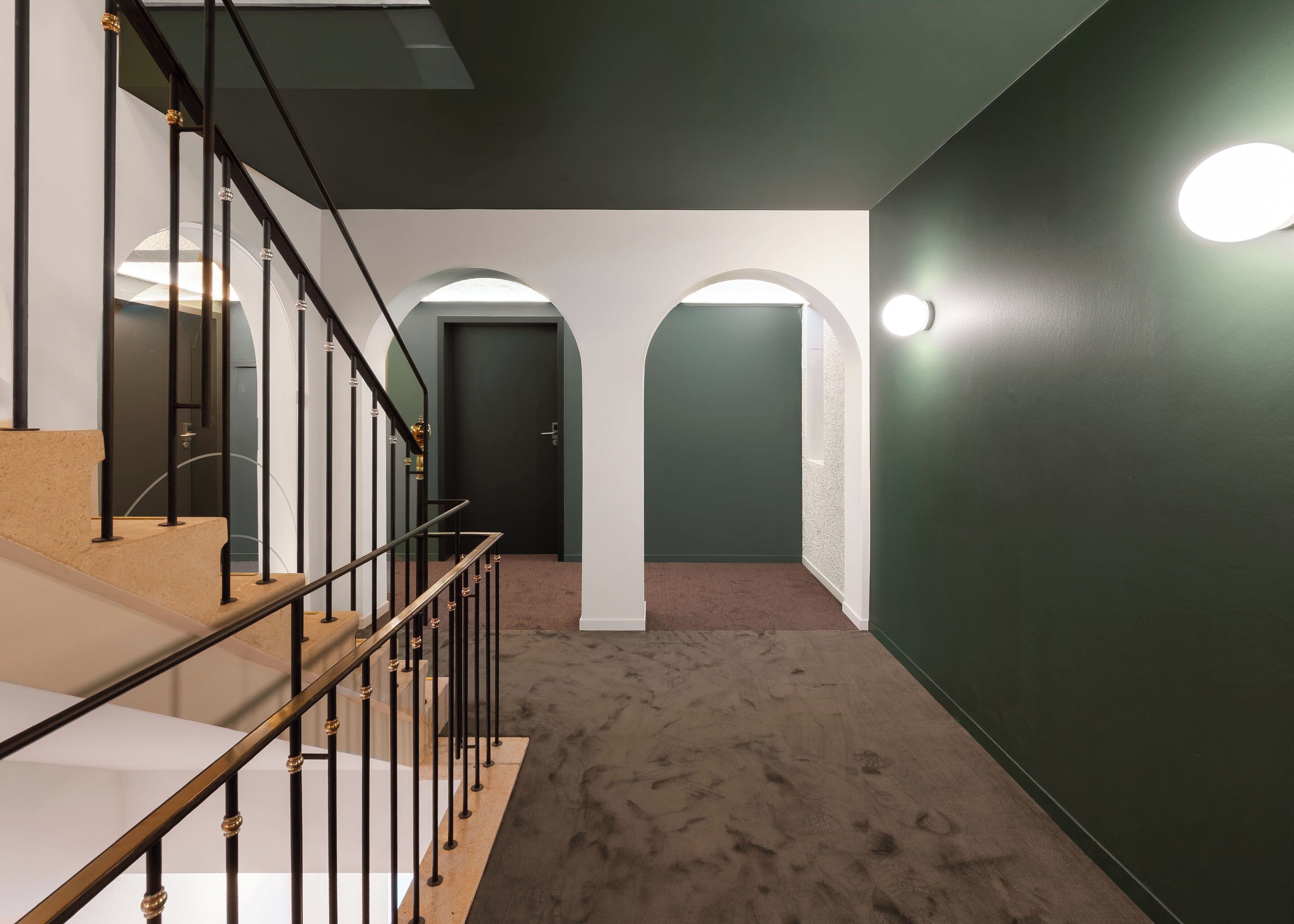 A hallway with a staircase, carpeted floor, and green walls.