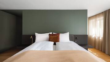 Une chambre d’hôtel avec un lit, une table de chevet, une commode et une fenêtre avec des rideaux.