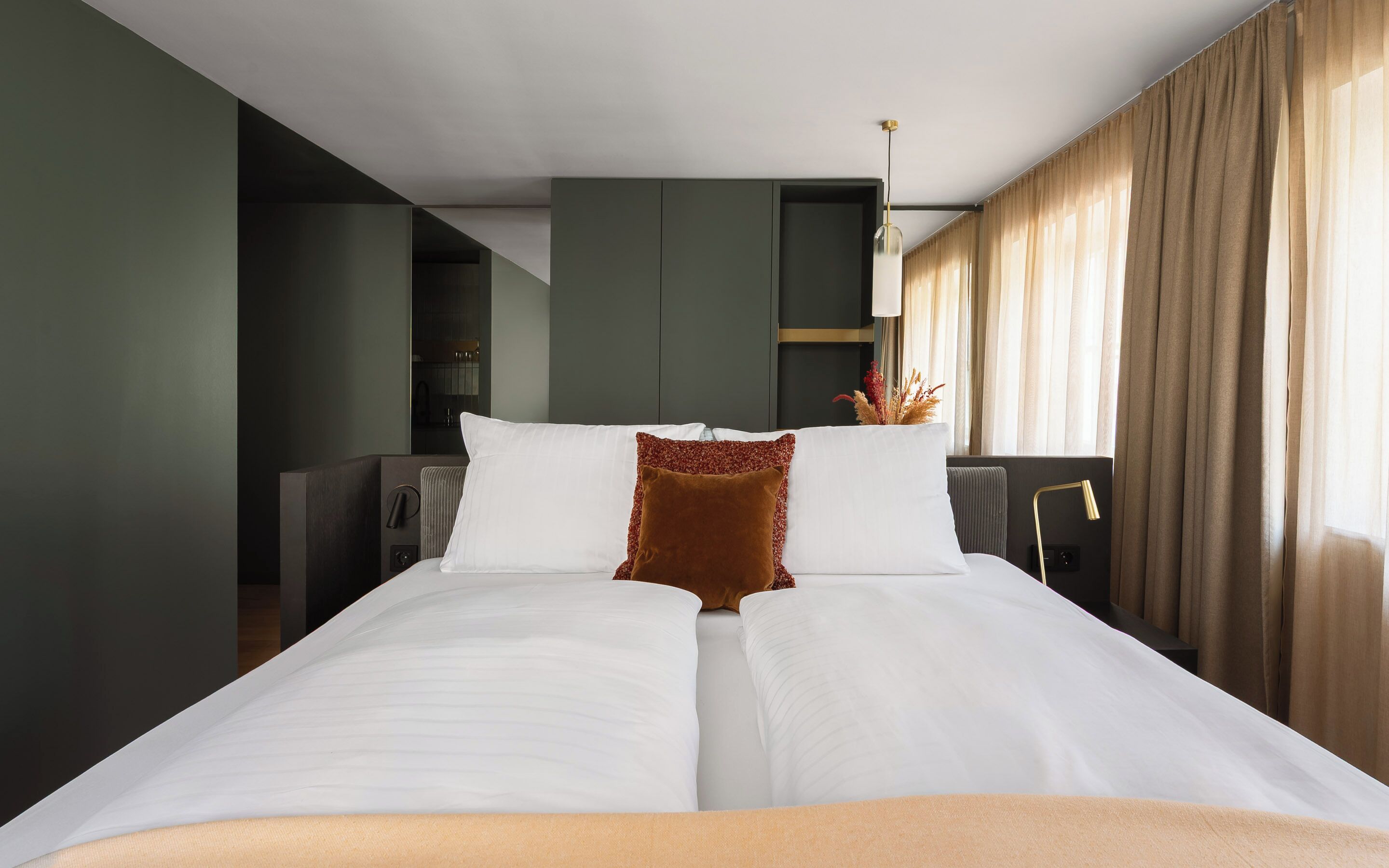 A hotel room with a large bed, a mirror, a radiator, and a view of the outside through curtains.