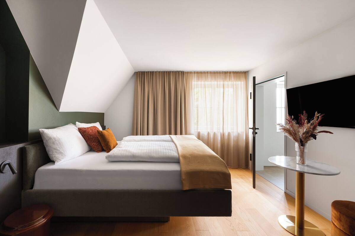 Ein modernes Schlafzimmer mit Bett, Nachttisch, Spiegel und einem Fenster mit Vorhängen.