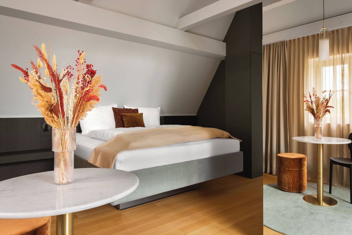 Ein modernes Hotelzimmer mit einem Bett, einem runden Tisch, einem kleinen runden Tisch und einer Vase mit Trockenblumen.