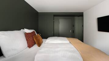 Une chambre d’hôtel moderne, équipée d’un lit, d’une porte et d’un téléviseur fixé au mur.