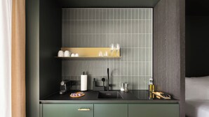 Una cocina compacta con diseño moderno, que incluye un lavamanos, una cafetera y una pequeña encimera con tabla de cortar y utensilios.