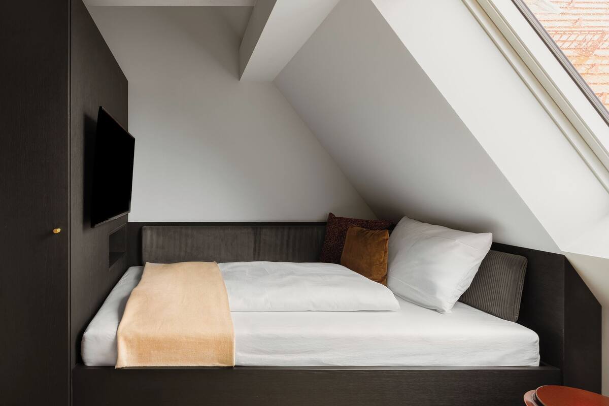 Ein modernes Schlafzimmer im Loft-Stil mit schrägem Dach, einem eingebauten Fernseher, einem Bett mit Kopfteil und einem kleinen Nachttisch.
