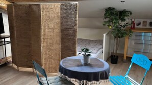 Ein Zimmer mit Oberlicht, einem Bett, einem Esstisch mit Stühlen, einer Topfpflanze und einer Küchenzeile.