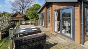 A modern outdoor patio with a glass table and wicker furniture, adjacent to a building with large sliding glass doors. - Borwick Heights 17 (Carnforth)