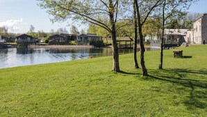 A riverside park with grassy areas, trees, and buildings in the background. - Borwick Heights 17 (Carnforth)
