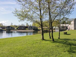Ein Flussuferpark mit Rasenflächen, Bäumen und Gebäuden im Hintergrund.