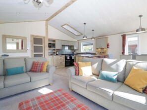 A spacious living area with a sofa set, a kitchen in the background, and a window with curtains. - Borwick Heights 17 (Carnforth)