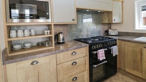 A kitchen with wooden cabinets, a microwave, a stove, and a toaster. - Borwick Heights 17 (Carnforth)