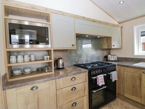 A kitchen with wooden cabinets, a microwave, a stove, and a toaster. - Borwick Heights 17 (Carnforth)
