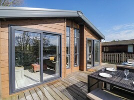 Um edifício moderno com grandes portas de vidro deslizantes, um deck de madeira e móveis de exterior.