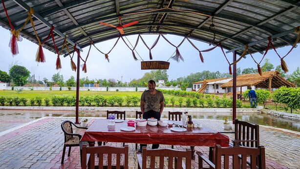 A covered outdoor dining area with a table set for two, surrounded by chairs, and a sign indicating 'Rajwada Farms.'
