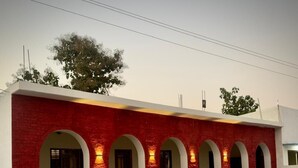 A building with red brick walls and white arches, a paved courtyard, and a white fence with square cutouts.