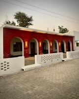 Un edificio con paredes de ladrillo rojo y arcos blancos, un patio empedrado y una cerca blanca con recortes cuadrados.