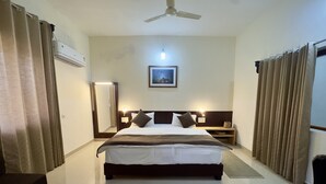 A hotel room with a bed, bedside tables, a ceiling fan, a wall-mounted air conditioner, and a framed picture on the wall.