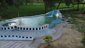 A swimming pool with a curved design, surrounded by a paved deck and a small garden area.