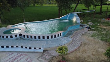 Una piscina de diseño curvo, rodeada por una solana pavimentada y un pequeño jardín.