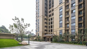 Un edifici residencial de diversos pisos amb balcons, un pati pavimentat i petits arbres.