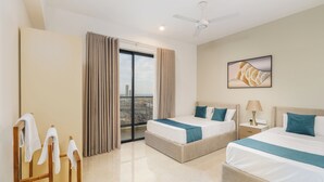 Una camera d'albergo con due letti, vista sulla città, una ventola a soffitto e un quadro appeso al muro.