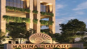 Un edificio con un cartello che indica 'MARINA SQUARE', con un grande logo a forma di conchiglia, balconi con giardino verticale e un design architettonico moderno.