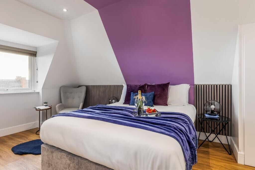Ein Schlafzimmer mit einem Bett, einem Nachttisch, einem Fenster und einer Wand in Lila.