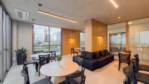 Un interior moderno con una mesa redonda, sillas negras, un sofá negro y ventanas amplias con vistas a la ciudad.