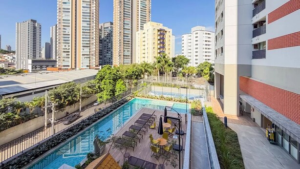 Un área de piscina en la azotea con sillones, una piscina y edificios altos al fondo.