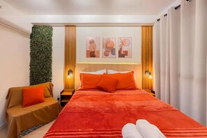 Quarto de hotel com cama, sofá, ar condicionado fixado na parede e parede com obras de arte emolduradas.