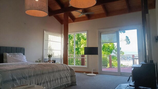 A bedroom with a bed, a standing lamp, a TV, and large windows. - Mountain view house (Trevallyn)
