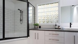 A modern bathroom with a glass shower enclosure, white tiled walls, a window with frosted glass, and a white sink with a black faucet. - Mountain view house (Trevallyn)
