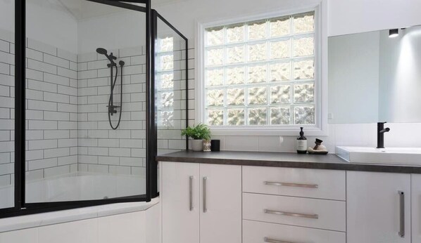 A modern bathroom with a glass shower enclosure, white tiled walls, a window with frosted glass, and a white sink with a black faucet. - Mountain view house (Trevallyn)