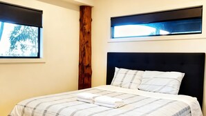A bedroom with a bed, a wooden accent wall, and windows with blinds. - Mountain view house (Trevallyn)