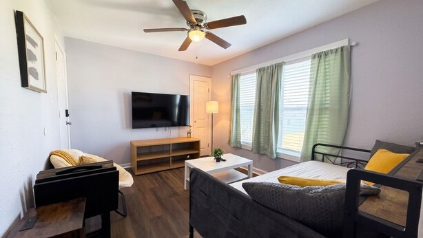A furnished room with a bed, a desk, a TV, a ceiling fan, and a window with curtains. - 2BDR+Extd Stay Discounts+Central+RemoteWork (Corpus Christi)