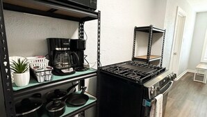 A compact kitchen with a microwave, stove, shelves with cookware, and a coffee maker. - 2BDR+Extd Stay Discounts+Central+RemoteWork (Corpus Christi)