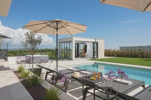 Ein Poolbereich im Freien mit Liegestühlen, einem Tisch und einem Sonnenschirm.