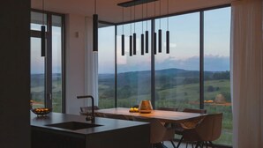 Eine moderne Küche mit einem großen Fenster, einem Essbereich mit Stühlen und einer hängenden Leuchte.