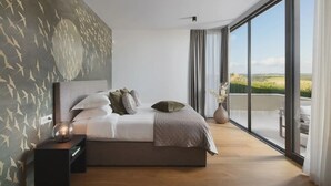Ein modernes Schlafzimmer mit einem großen Bett, einem Nachttisch, einer Wandmalerei, einem großen Fenster und Blick auf die Landschaft.