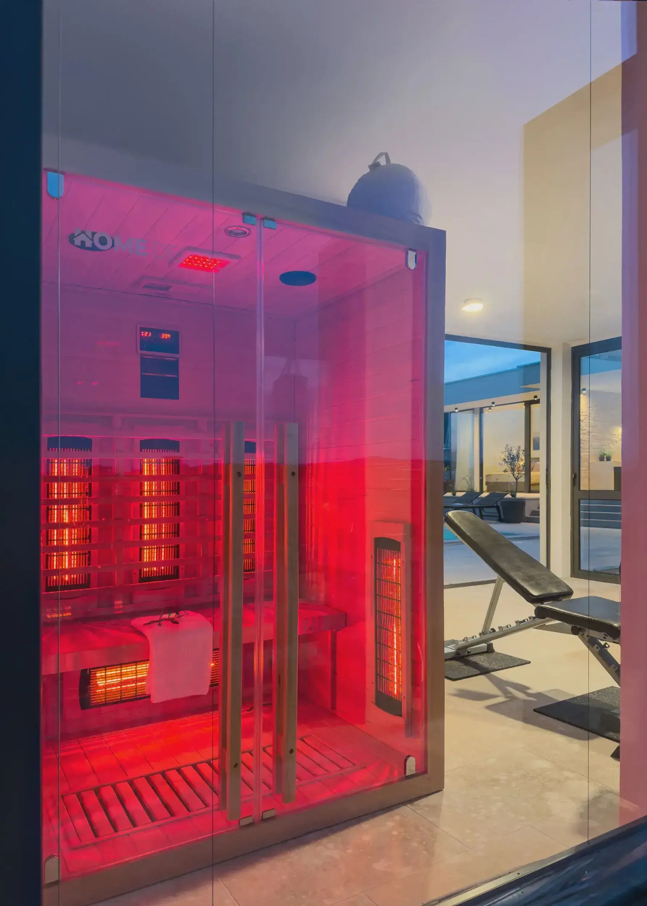 A sauna with glass walls, a bench, and a digital display.