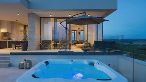 Ein moderner Außenbereich mit Whirlpool, Glasgeländern, einer Sitzecke mit Stühlen und Tisch sowie Blick auf die Landschaft.
