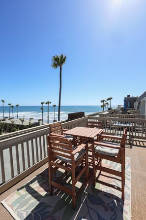 Une terrasse en bois avec une table et des chaises, donnant sur une plage bordée de palmiers et sur l’océan.